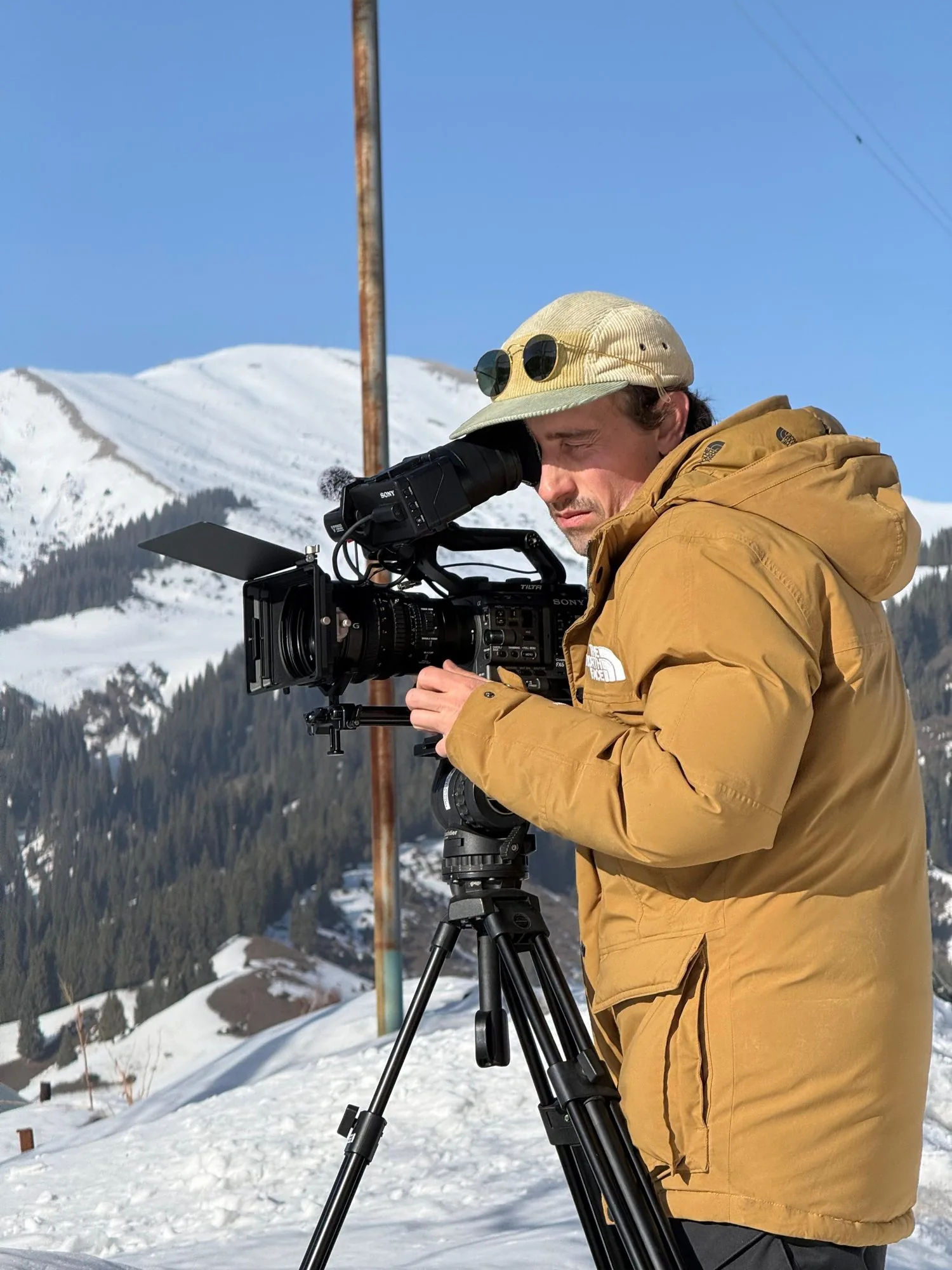 Frederic T. Kuntz looking through the viewfinder of a camera on a tripod in the snowy mountains